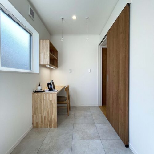 広々4帖のサンルームの一角にはミシン掛けやアイロンがけができる造作デスクと棚を設置。こちらの床は、サンゲツの石目調のフロアタイル（IS-938）を使用。サンルームは奥様専用の趣味のお部屋も兼ねています。