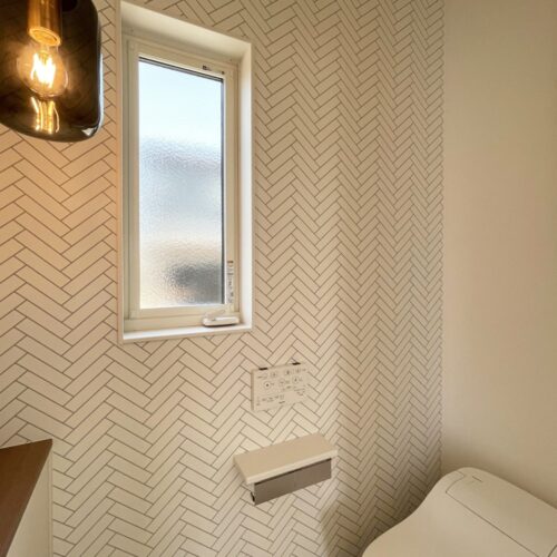 スモークガラスの中のポワンとした明りが印象的なペンダントライト（DAIKO DPN-41363Y）と、ヘリンボーン柄のアクセントクロス（サンゲツ FE-74175）がとってもおしゃれな空間を演出してくれるトイレ。  アクセントクロスを入れつつも、全体的にホワイトでまとめられています。