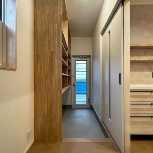 キッチン奥の扉を開けると勝手口へと繋がります。  勝手口には、食品や日用品のストックをたっぷり収納できるように可動棚を造作しました。  お買い物後は勝手口から入り、サッと収納！料理中も必要な食材を、サッと取ることができます♪