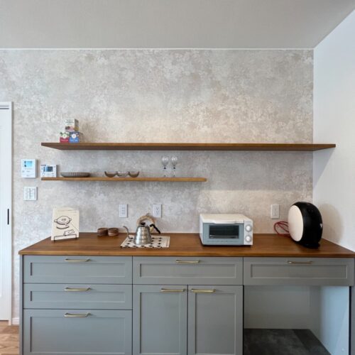 キッチン背面のカップボードはウッドワンをチョイス(*^^*)  本体カラーはグレー、取手はゴールドを選ばれました。  木×グレー×ゴールドのバランスがお洒落の極みですね★     カップボード：ウッドワン スイージー W2295  棚：大工さんのお手製  アクセントクロス：リリカラ LL-5079