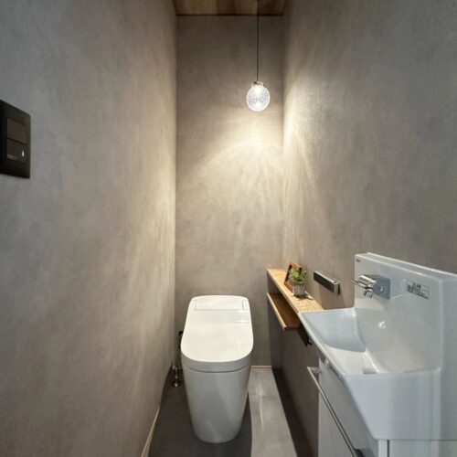 グレーを基調としたトイレ空間です。  天井には木目調のクロスをアクセントに。  ほわほわっとやわらかいペンダントライトの光が落ち着く空間を演出してくれています。