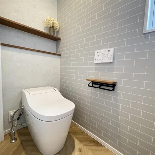 ヘリンボーン柄の床材とレンガ調のクロスがお洒落なトイレ♪  トイレの背面にはオープンタイプの造作棚を設けました！トイレットペーパーなどの収納品も出し入れがスムーズです。