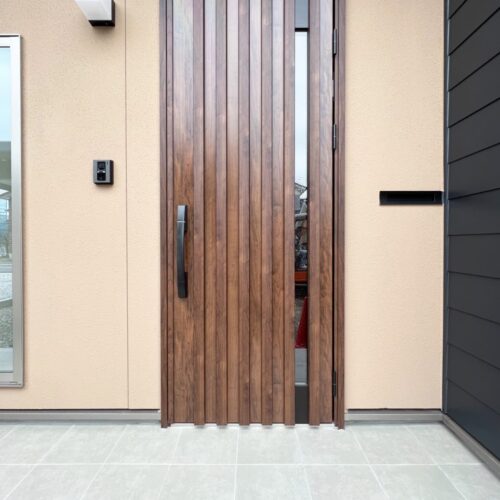 玄関ポーチは、外壁のブラック系の金属サイディングに合わせて、吹付塗装でアクセントを付けました。  玄関ドアは、YKKのヴェナートを。  ガナッシュウォールナットというお色を選ばれました(^^)細くガラスが入っていることで光が取り込まれ、玄関も明るくなります◎