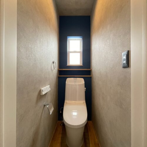 二階のトイレです。  モルタル調のクロスに背面はネイビーのクロスをアクセントに！  トイレットペーパーを収納できる幅の棚を設けてあります。