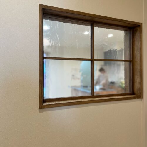 玄関ホールとリビングをつなげる室内窓。揺らめく水面を思わせるようなアンティークガラスとブラウンの窓枠がやさしく光を取り込みます。